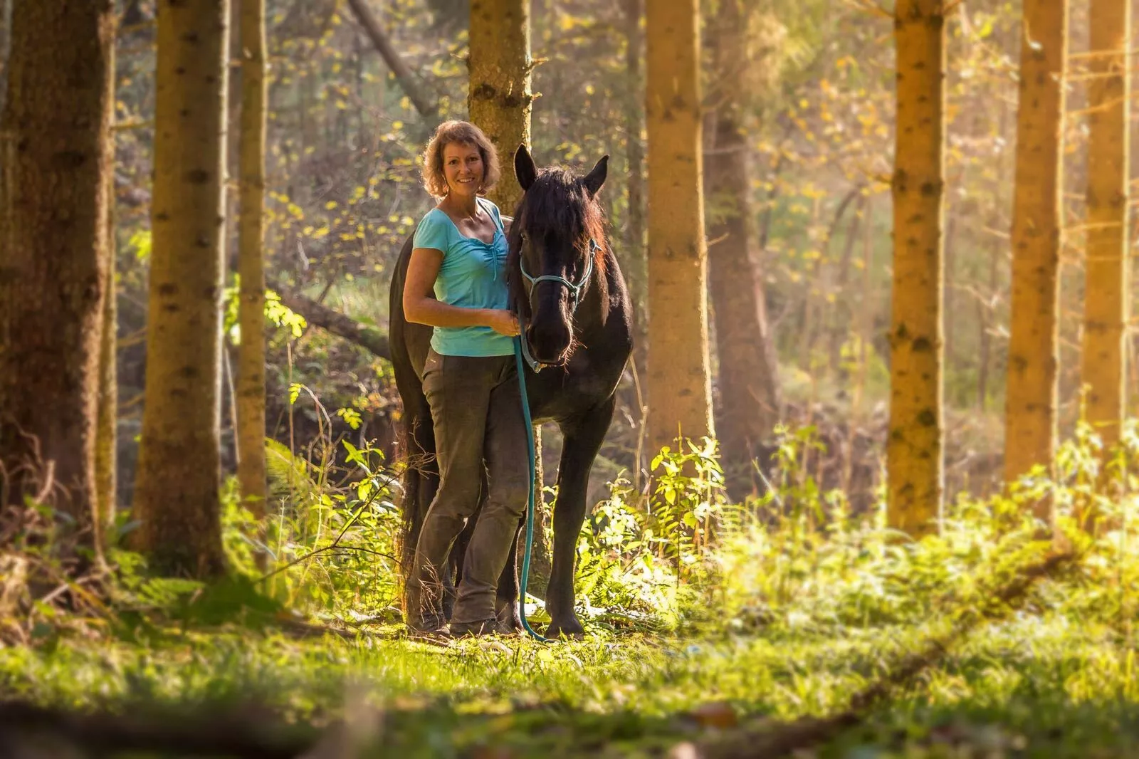 Sabine Junginger mit ihrem Pferd im sonnendurchfluteten Wald